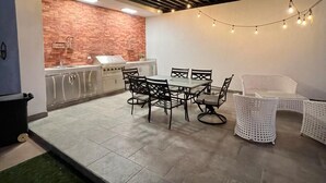 Un patio al aire libre con pared de ladrillo, zona de cocina y juego de comedor.