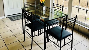 A dining area with a glass table and black chairs, a white door, and a window with a view of greenery.