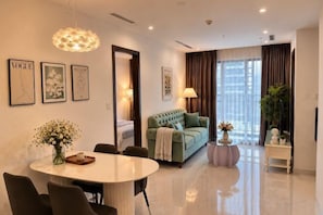 A modern living room with a round dining table, a green sofa, and a large window with curtains.