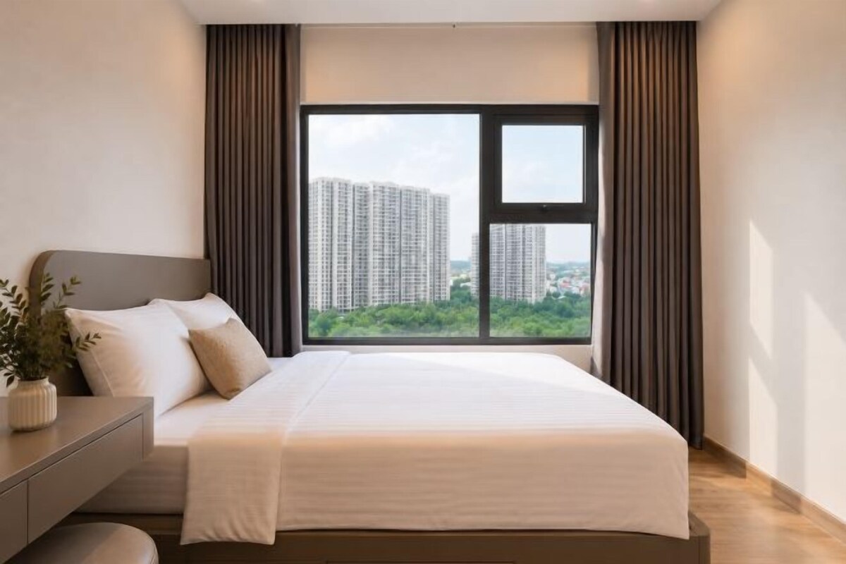 Ein modernes Hotelzimmer mit einem großen Bett, einem Nachttisch, einer Topfpflanze und Blick auf hohe Gebäude.