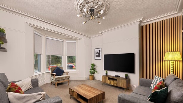 A living room with a flat-screen TV, grey sofas, a wooden coffee table, and a large window. - 6 Bedroom Victorian Terrace, 3.5 baths (Hensingham)