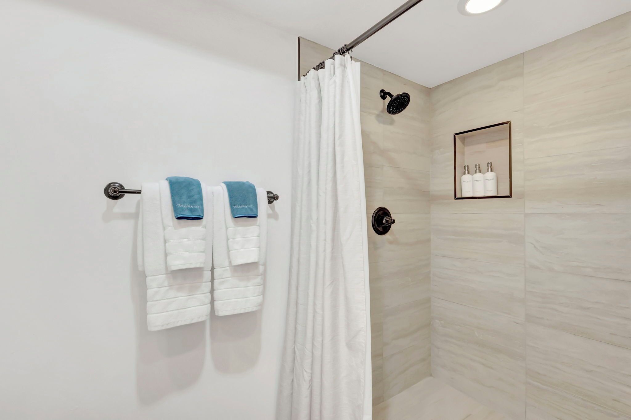 A modern shower area with a glass door, white towels, and a framed picture of toiletries.