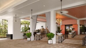 A spacious lobby with a modern design, featuring a central staircase, potted plants, and a view of the outdoors.