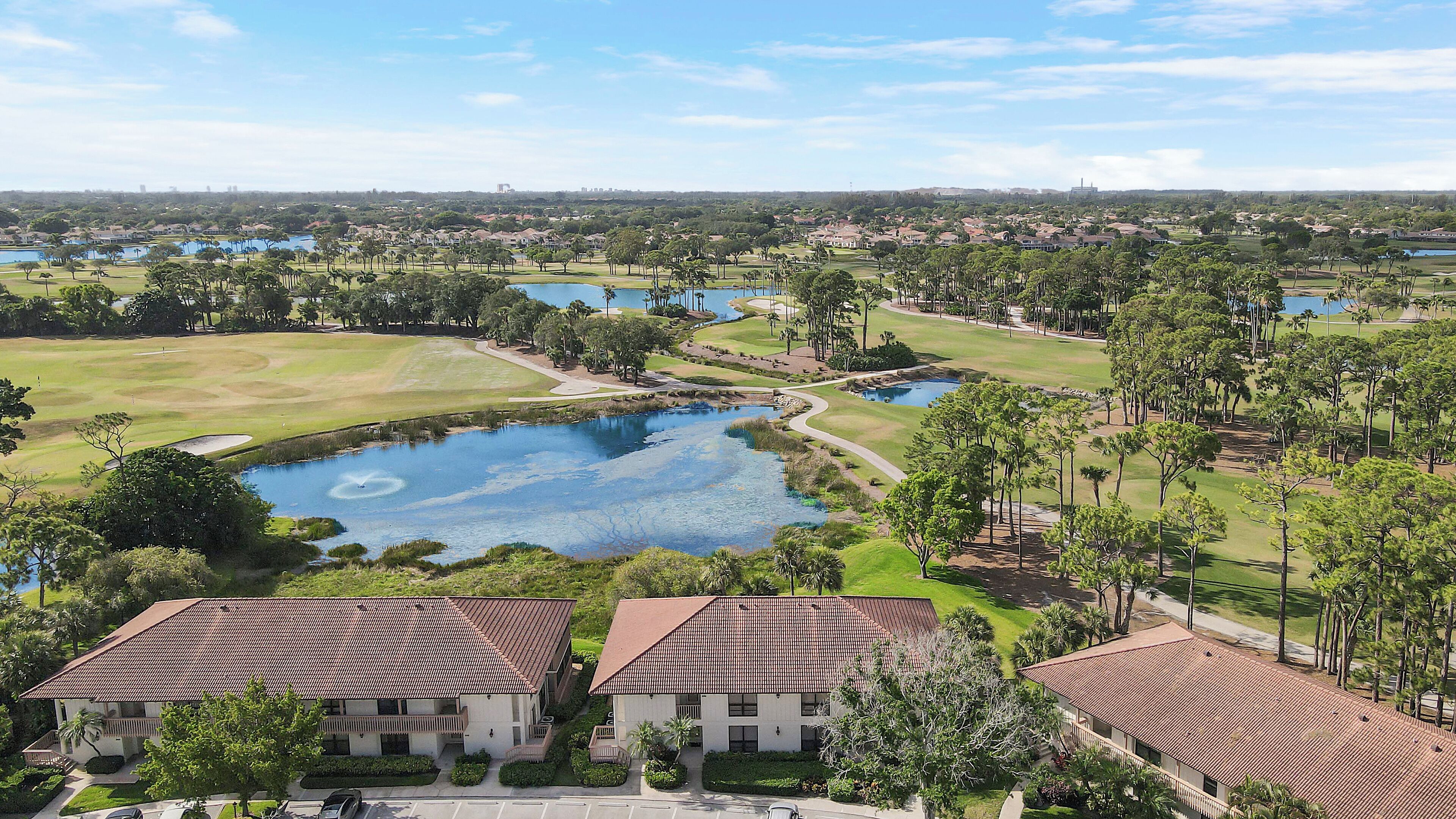 Campo de golf con un estanque, rodeado de edificios residenciales con techos de tejas rojas.