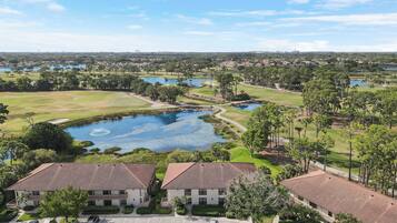 Campo de golf con un estanque, rodeado de edificios residenciales con techos de tejas rojas.