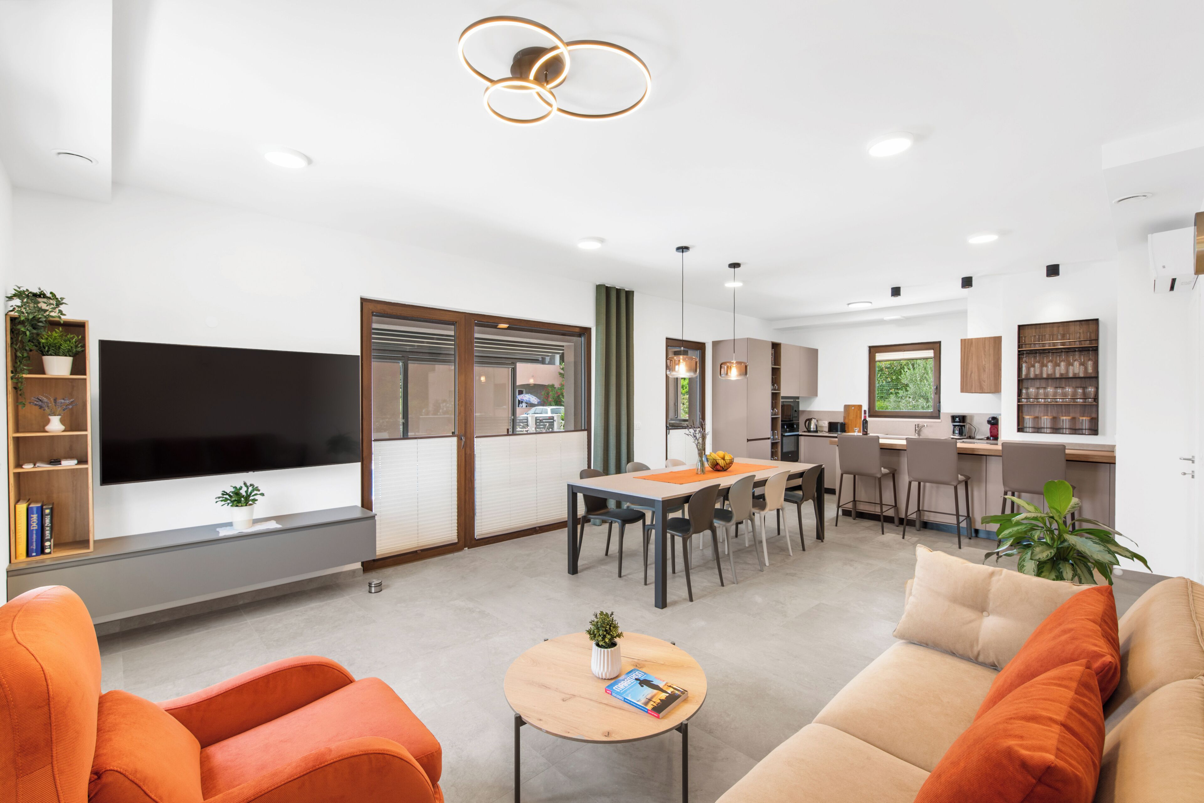 Un salon moderne doté d’un téléviseur à écran plat, de canapés orange, d’un coin repas et d’une cuisine.