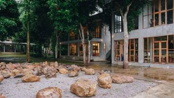A building with a courtyard, large rocks, trees, and a gravel path.