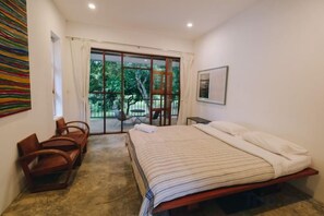 A bedroom with a bed, a chair, a table, and a view of the outdoors through a sliding door. - Loogmai Guesthouse (Chiang Khan)