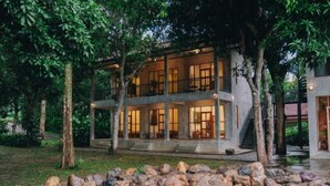 A two-story building with a balcony, surrounded by trees and a rock garden. - Loogmai Guesthouse (Chiang Khan)