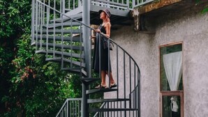 A person standing on a spiral staircase attached to a building with a window and a door. - Loogmai Guesthouse (Chiang Khan)