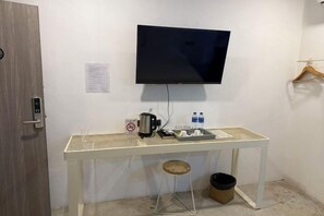 A room with a white desk, a mounted TV, a coffee maker, and a trash bin. - G Lighthouse (Chiang Mai)