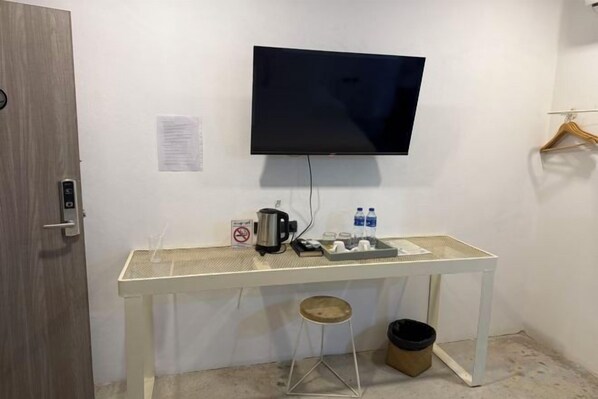 A room with a white desk, a mounted TV, a coffee maker, and a trash bin. - G Lighthouse (Chiang Mai)