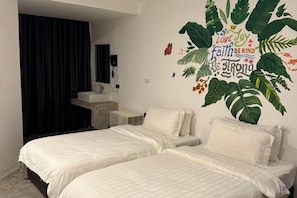 Camera d'albergo con due letti, bagno con lavandino e un murale raffigurante foglie tropicali e testo.
