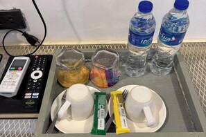 A tray with two cups, two bottles of water, a remote control, and some food packets. - G Lighthouse (Chiang Mai)