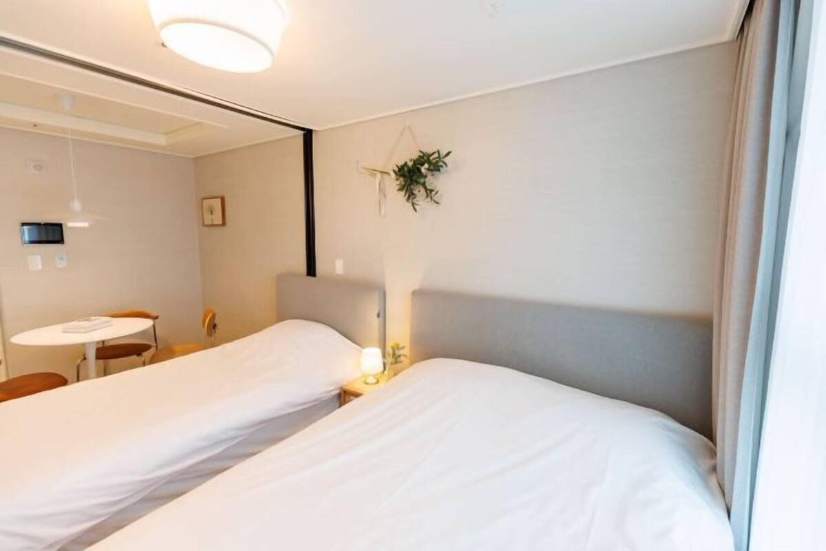 Une chambre d’hôtel avec deux lits, une petite table, une chaise, une lampe de chevet et une plante accrochée au mur.