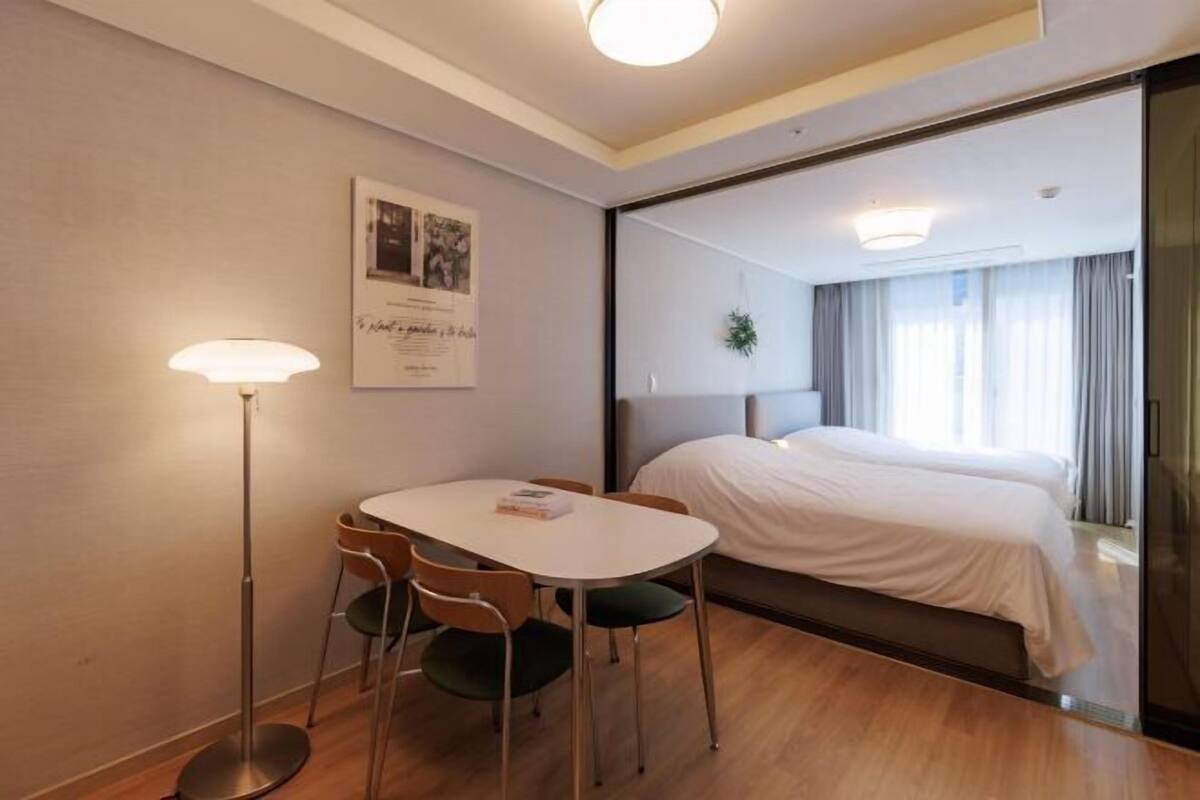 Une chambre d’hôtel avec un lit, une table et des chaises, une lampe sur pied et un tableau encadré au mur.