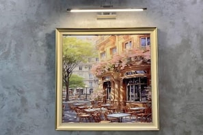 A framed painting of a café scene with outdoor seating and a building facade.