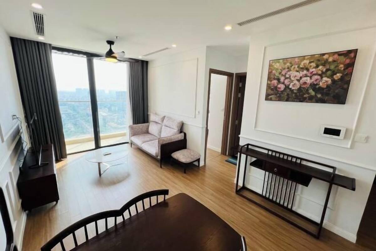 A modern living room with a sofa, a dining table, a TV, and a painting on the wall.