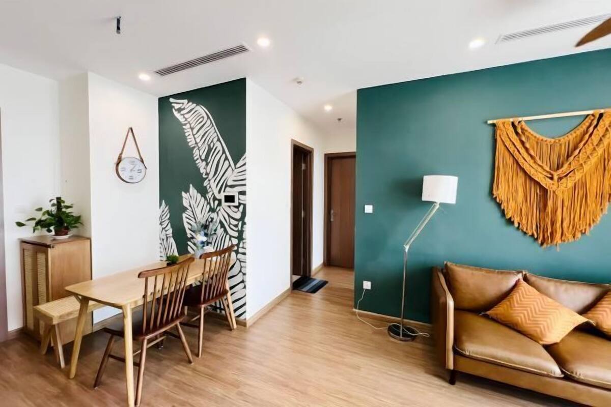 A modern living room with a wooden dining table, a sofa, and a green accent wall.