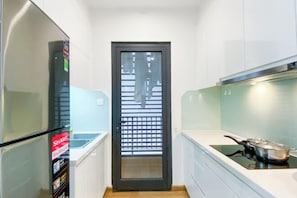 A narrow kitchen with white cabinets, a black-framed door with a grid pattern, and a stove with a pot on it.