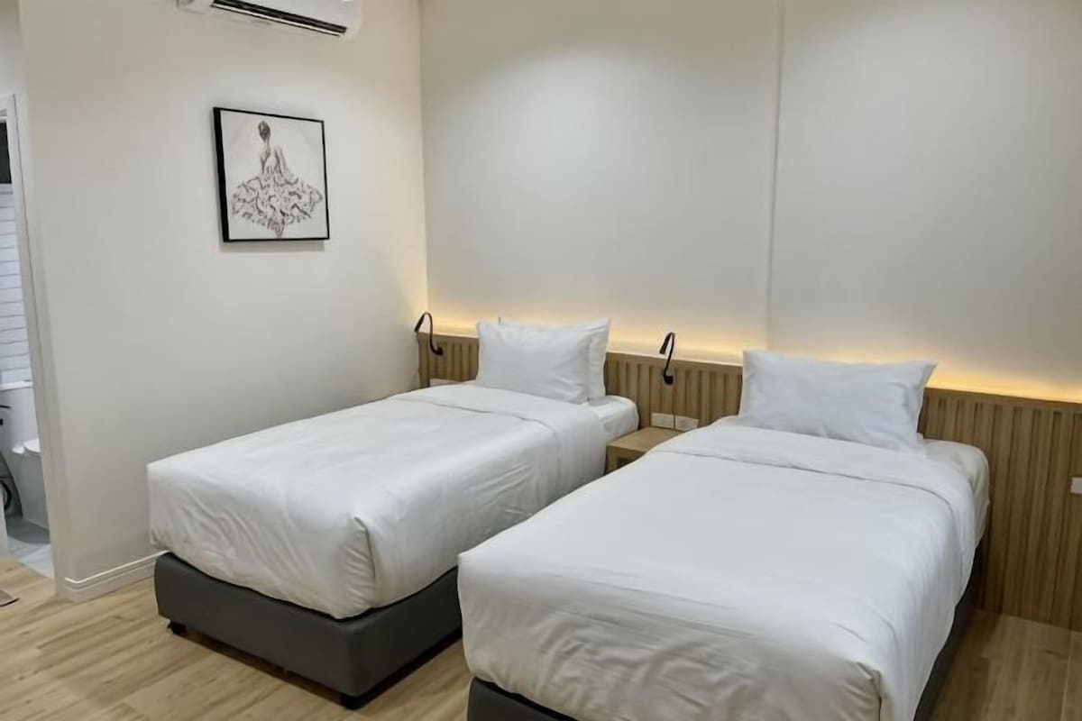 A hotel room with two single beds, a framed picture on the wall, and a wooden floor.