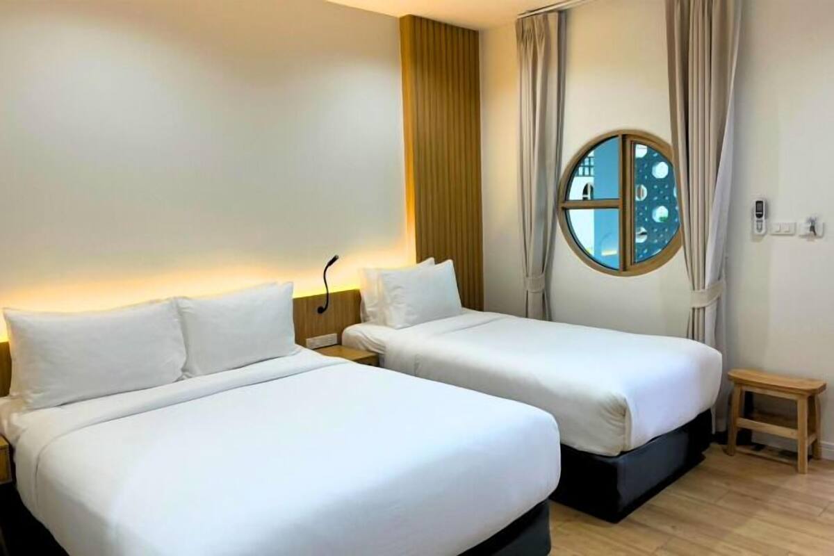 Une chambre d’hôtel avec deux lits, une petite table de chevet, une fenêtre ronde donnant sur le paysage et une lampe fixée au mur.