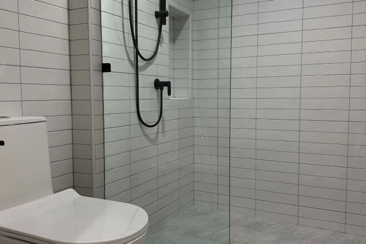 A bathroom with white tiled walls, a white toilet, and a shower area with a black hose.