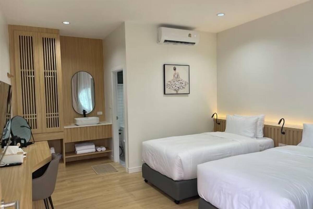 Une chambre d’hôtel avec deux lits, un bureau avec une chaise, un miroir, un lavabo et un appareil de climatisation.