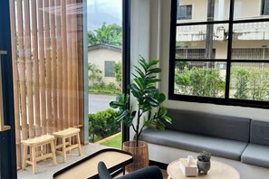 A modern room with a large window, a sofa, a small table, and a plant. - Mani Ranong Hotel (Ranong)