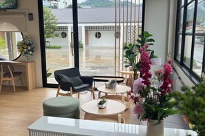 A modern interior with a seating area, a small table, and a view through a glass door. - Mani Ranong Hotel (Ranong)