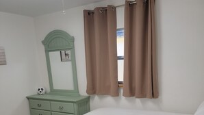 Une chambre à coucher avec un lit, une commode verte, un miroir et des rideaux marron.