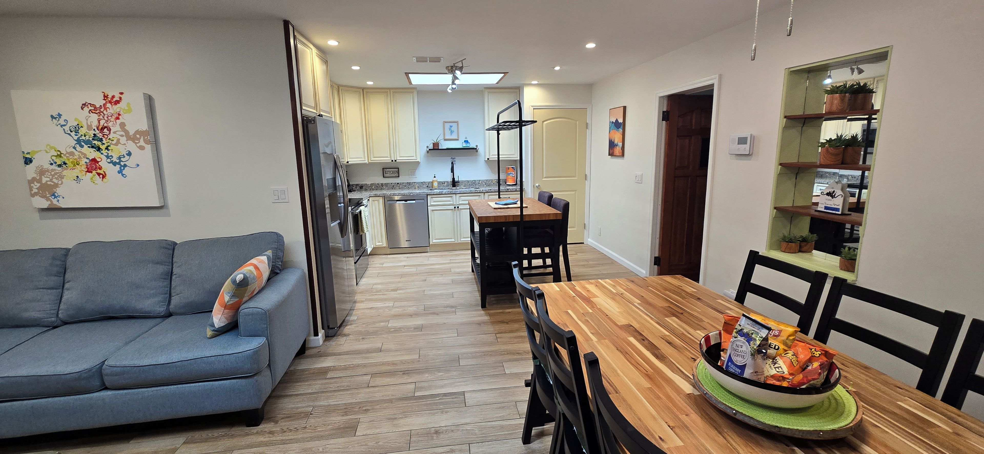 A modern kitchen with white cabinets, a wooden dining table, and a blue sofa.