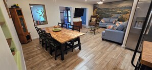 Un coin repas avec une table et des chaises en bois, un canapé, une télévision et un réfrigérateur.