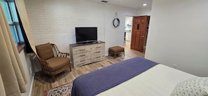 Une chambre à coucher avec un lit, un téléviseur posé sur une commode, une chaise et un petit tabouret.