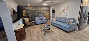 Un salon comprenant deux canapés, une table basse, une cheminée et une grande fresque représentant un paysage montagneux.