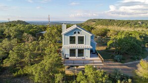 A two-story house with a balcony, surrounded by trees and a hilly landscape. - Cliffside at Canyon Lake - Monthly Rental (New Braunfels)