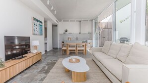 A modern living room with a TV, sofa, coffee table, and dining area. - Salt & Stone Luxe Hideaway Byron Bay (Byron Bay)