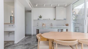 A modern kitchen with white cabinets, a marble countertop, and a dining area with a wooden table and chairs. - Salt & Stone Luxe Hideaway Byron Bay (Byron Bay)