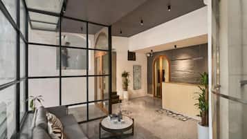 A modern interior with a glass partition, a seating area with a sofa, a coffee table, and potted plants.