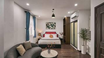 Una habitación de hotel moderna con un sofá curvo, una mesa de centro redonda, una cama grande con cabecera roja y una obra de arte abstracta colgada en la pared.