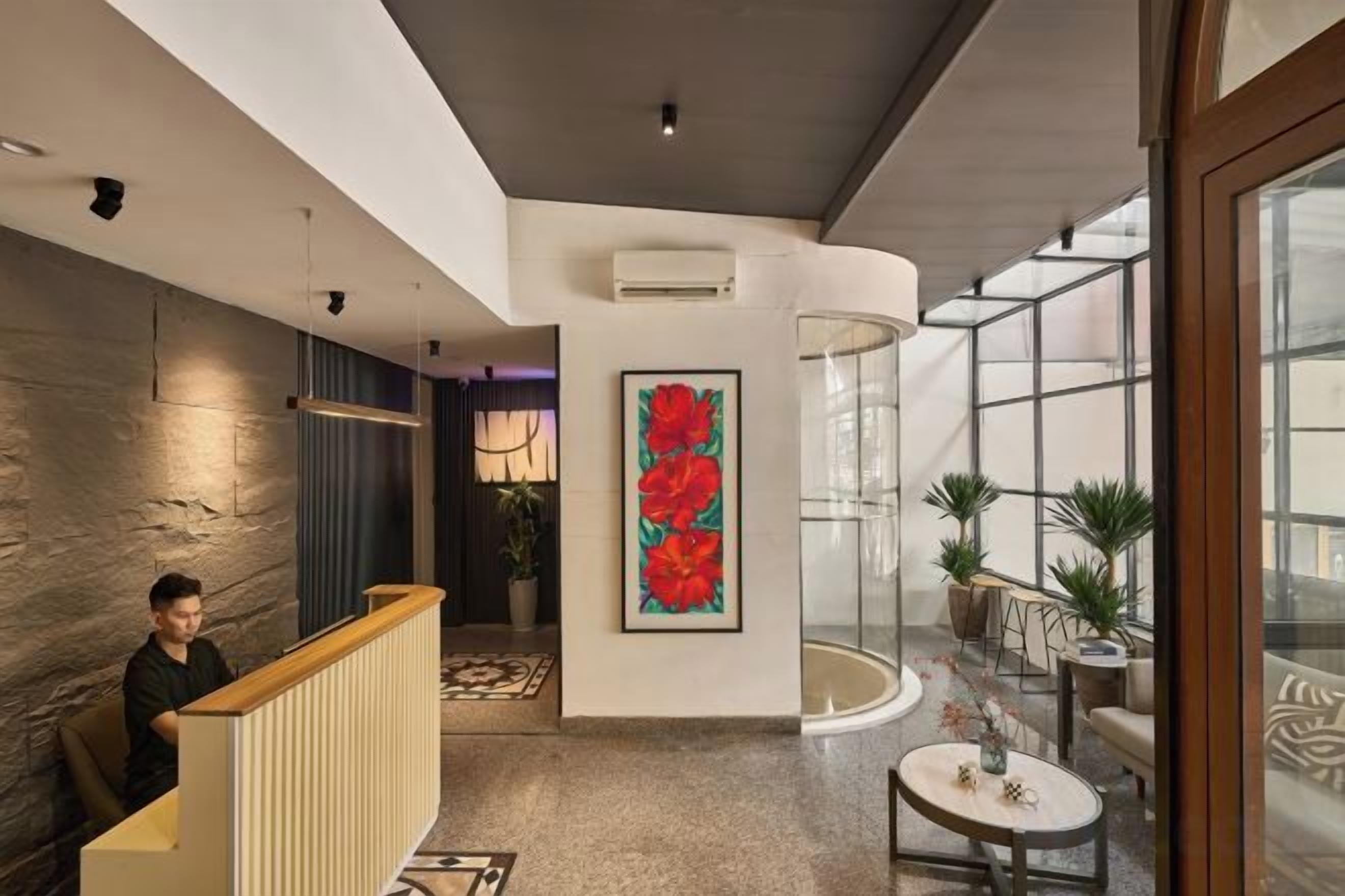 Un moderno vestíbulo de hotel con un mostrador de recepción, una gran obra de arte floral, una estructura de vidrio y plantas en macetas.