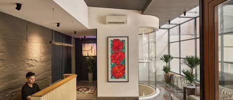 Un moderno vestíbulo de hotel con un mostrador de recepción, una gran obra de arte floral, una estructura de vidrio y plantas en macetas.