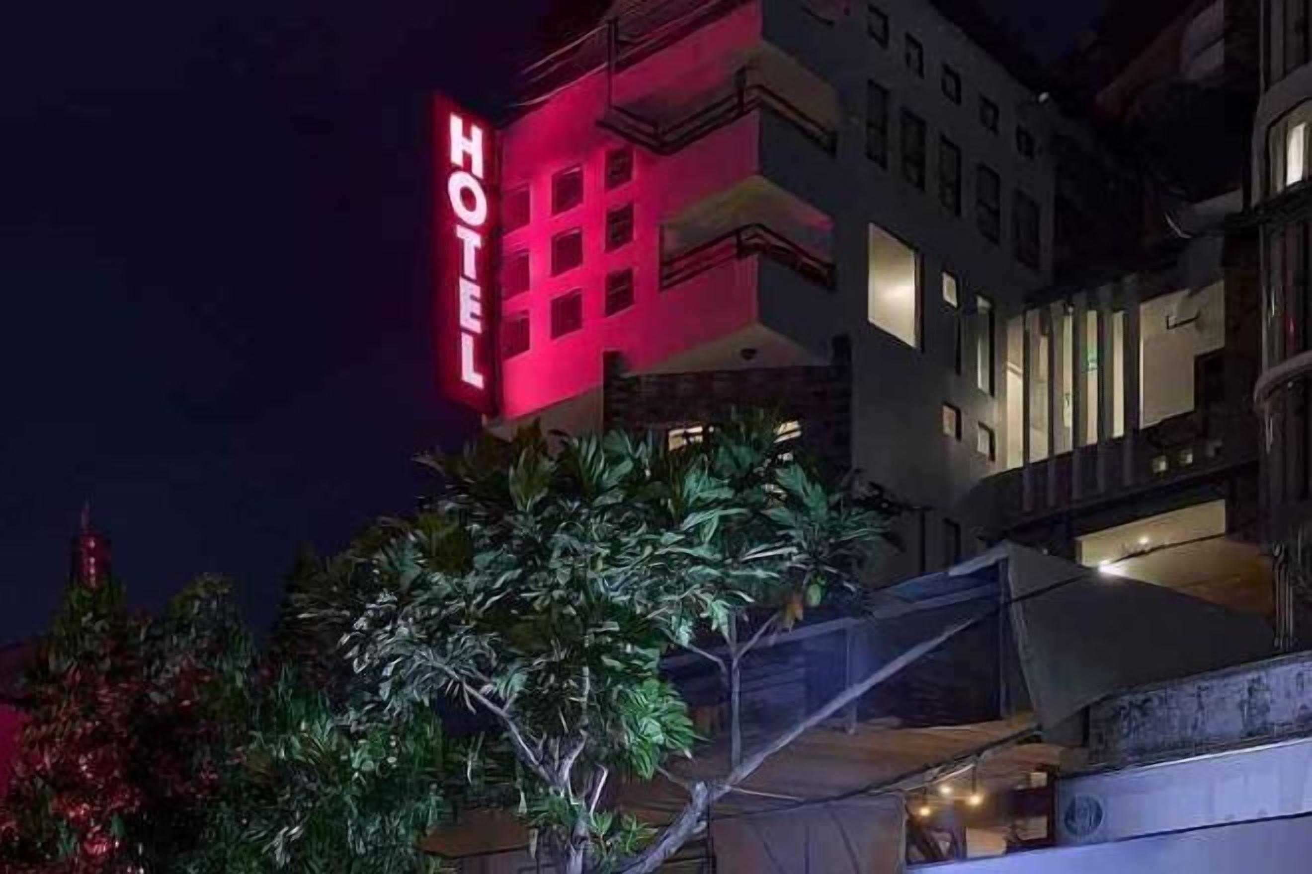 A hotel with a prominent red sign, a modern architectural style, and a well-lit facade.