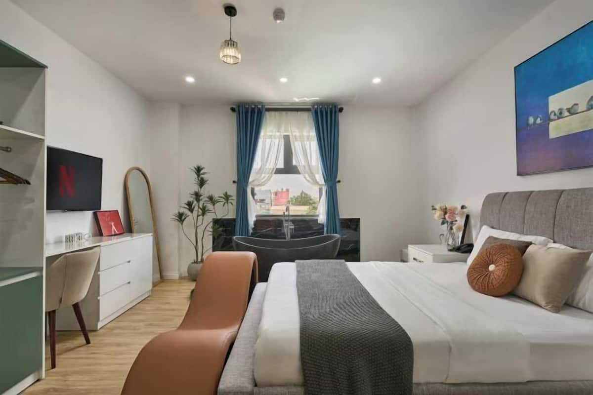 A modern bedroom with a bed, a desk, a chair, a bathtub, and a large window with curtains.