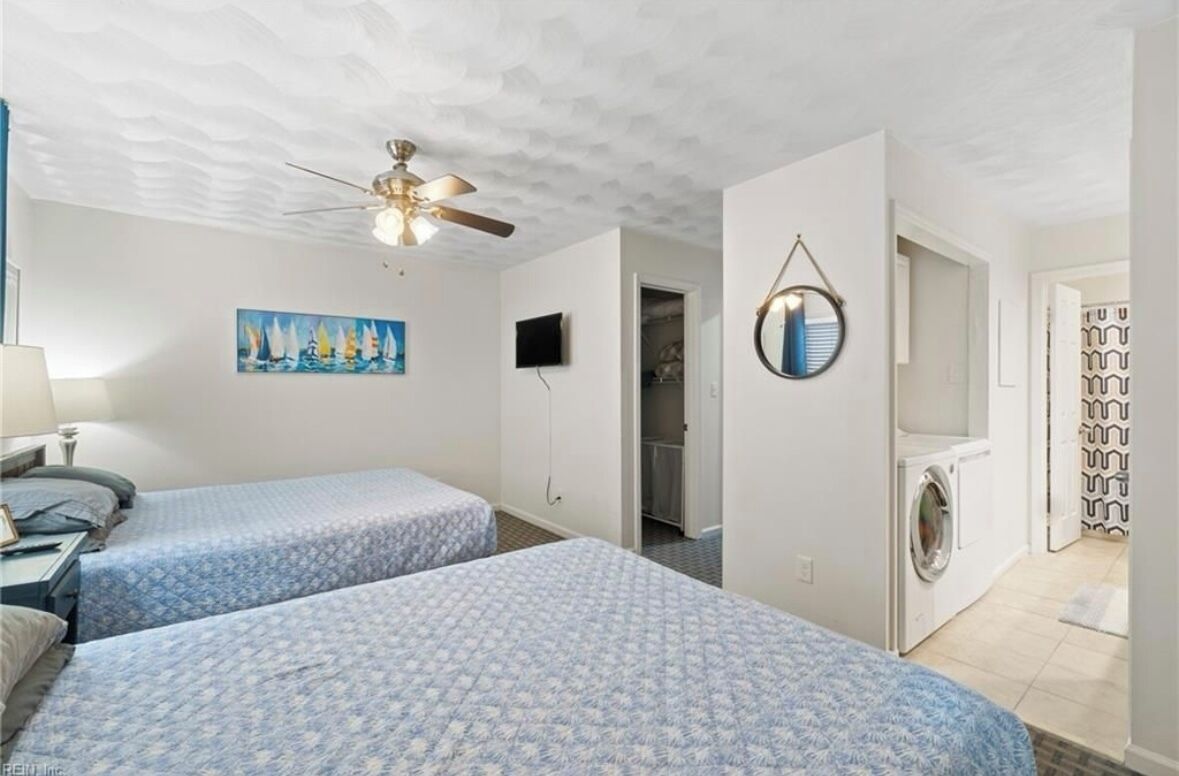 Una habitación con dos camas, ventilador de techo, un cuadro, televisión, espejo y lavadora.