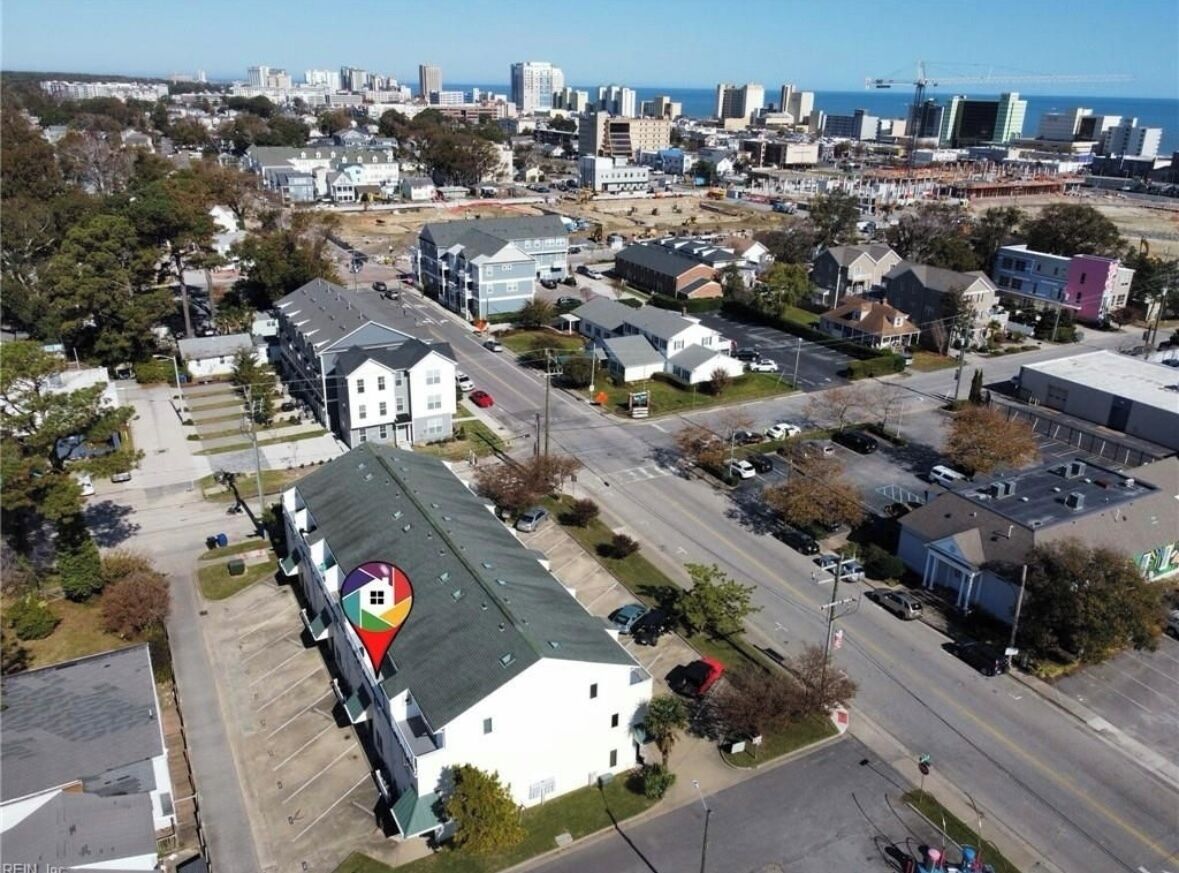 Vista aérea de una zona residencial con un gran edificio blanco de techo verde, rodeado de casas más pequeñas y una calle.