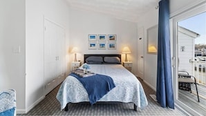 A bedroom with a bed, two bedside tables with lamps, a window with a view, and a ceiling fan. - Vibe District, Atlantic Surf Park, VB Sports Center, Boardwalk & Oceanfront (Virginia Beach)