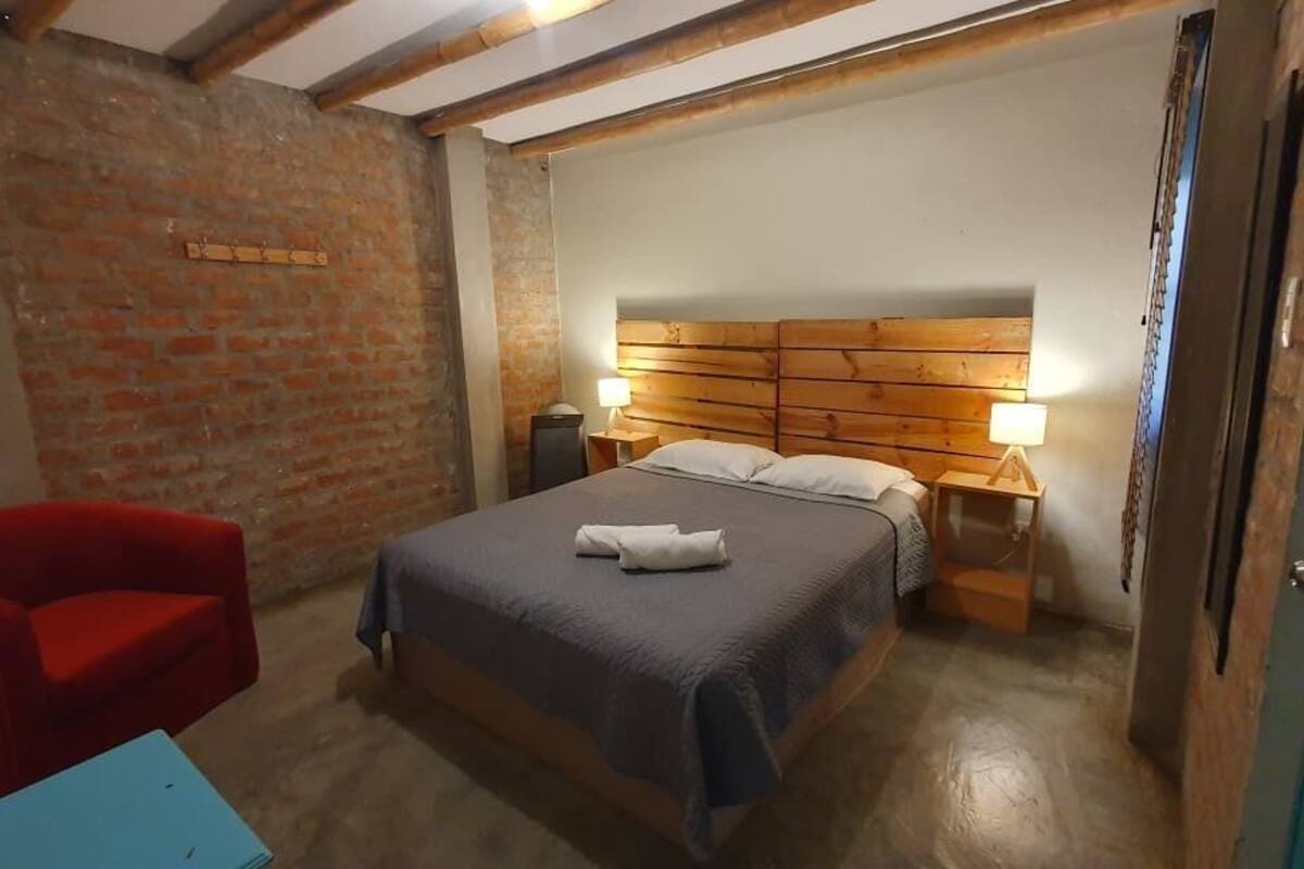 A bedroom with a wooden headboard, a bed with a blue blanket, two bedside lamps, a red chair, and a wooden door.