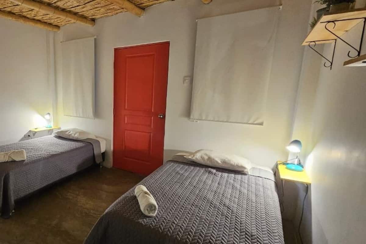 A room with two beds, a red door, and a red chair.