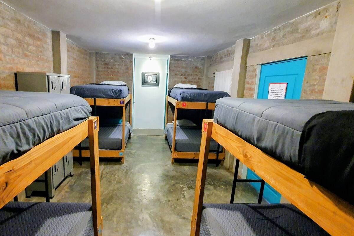 A dormitory room with bunk beds, a small desk, and a blue door.